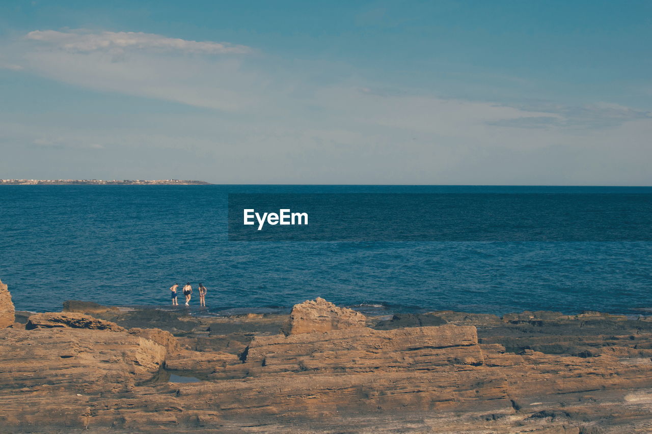 ROCKS BY SEA AGAINST SKY