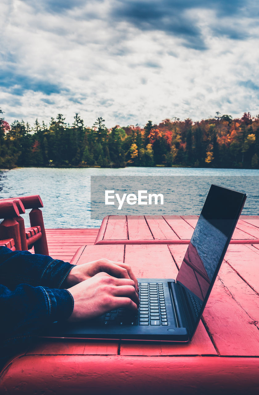 A freelance male taking outdoors in autumn, laptop by the lake. blurred bkgrd - aged effect filtered