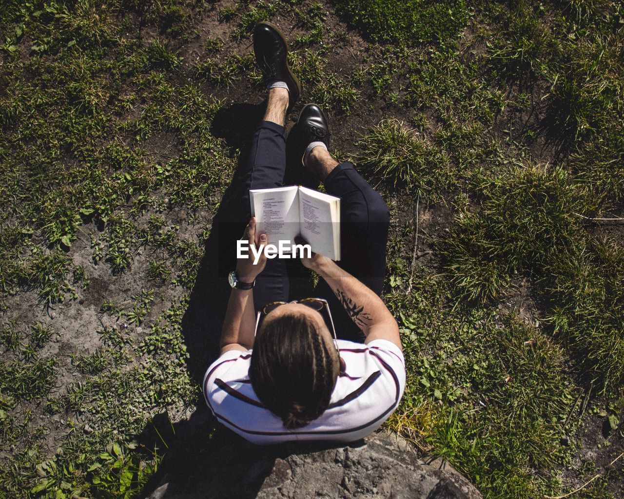 High angle view of man reading book while sitting on grassy field