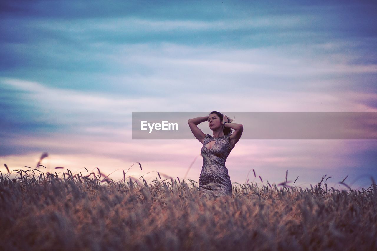 Low angle view of woman standing on wheat field against cloudy sky during sunset