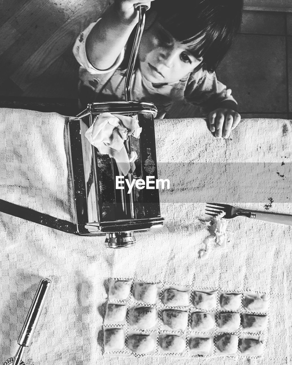 High angle view of boy holding pasta maker by ravioli on table