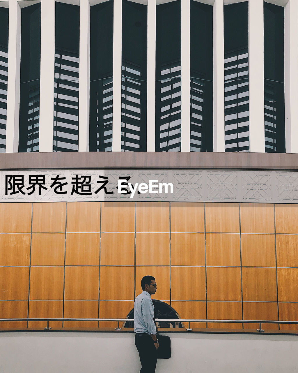 FULL LENGTH OF MAN STANDING AGAINST RAILING IN CITY