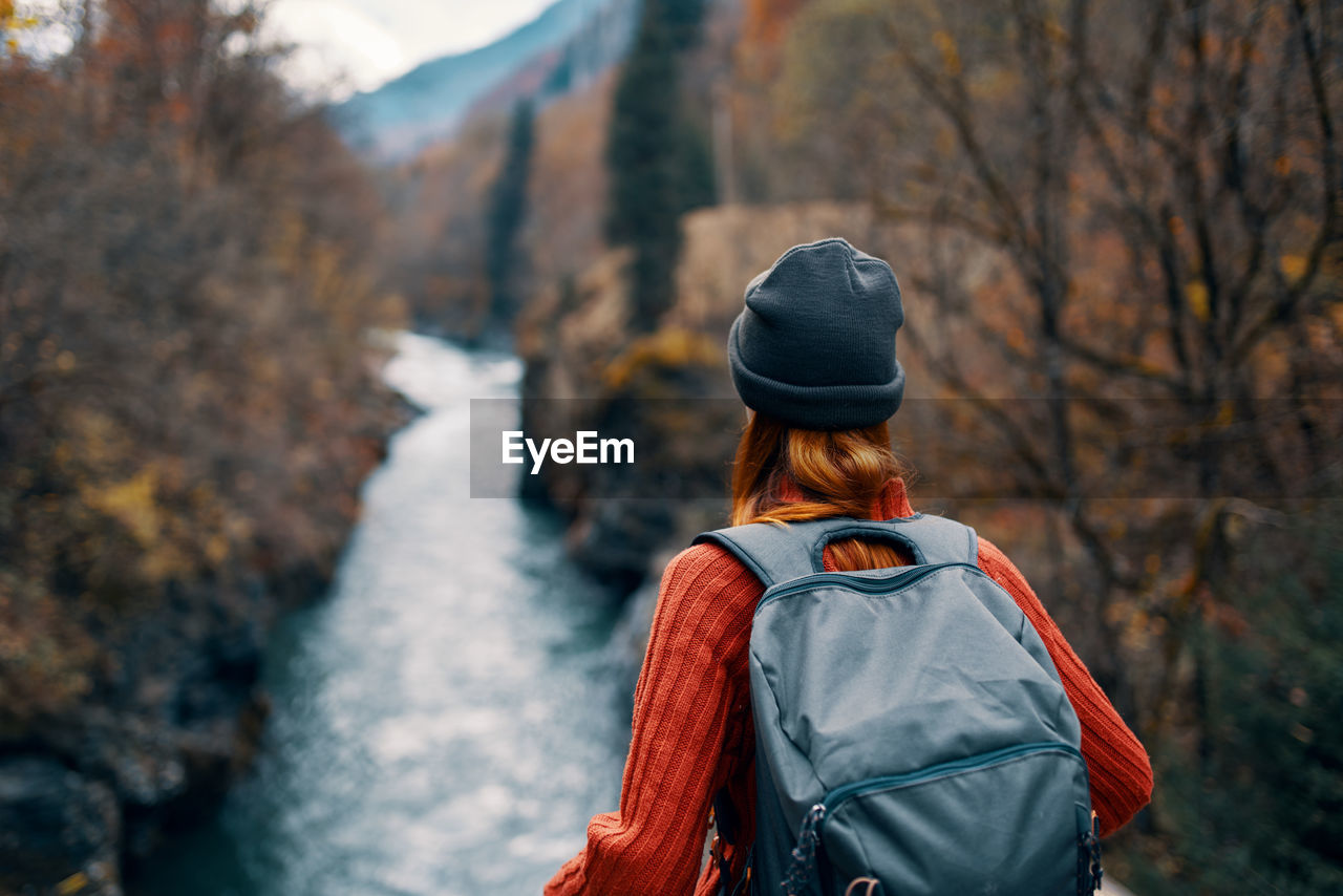 REAR VIEW OF WOMAN LOOKING AT FOREST DURING AUTUMN