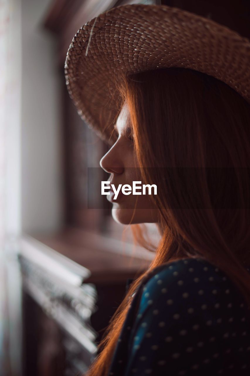 Side view of young woman wearing hat at home