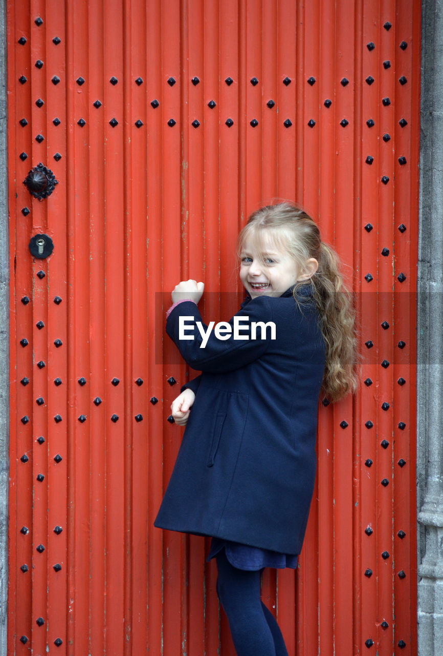 Portrait of cute girl standing against red door