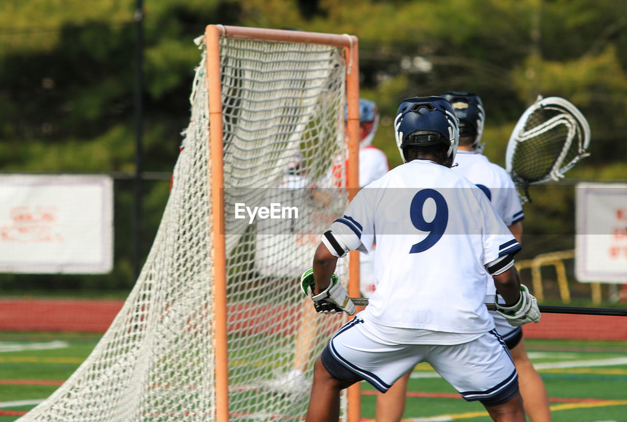 sports, ball game, athlete, player, lacrosse, team sport, clothing, competition, sports uniform, adult, sports equipment, young adult, rear view, sports clothing, activity, men, motion, one person, ball, scoring, outdoors, playing field, net - sports equipment