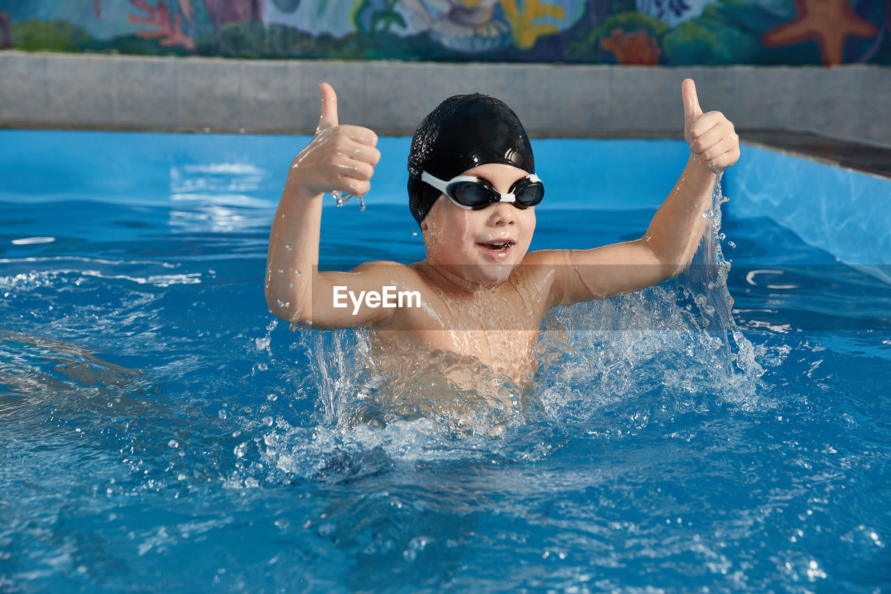 Preschool boy learning how to swim in a pool wearing swimming cap and goggles