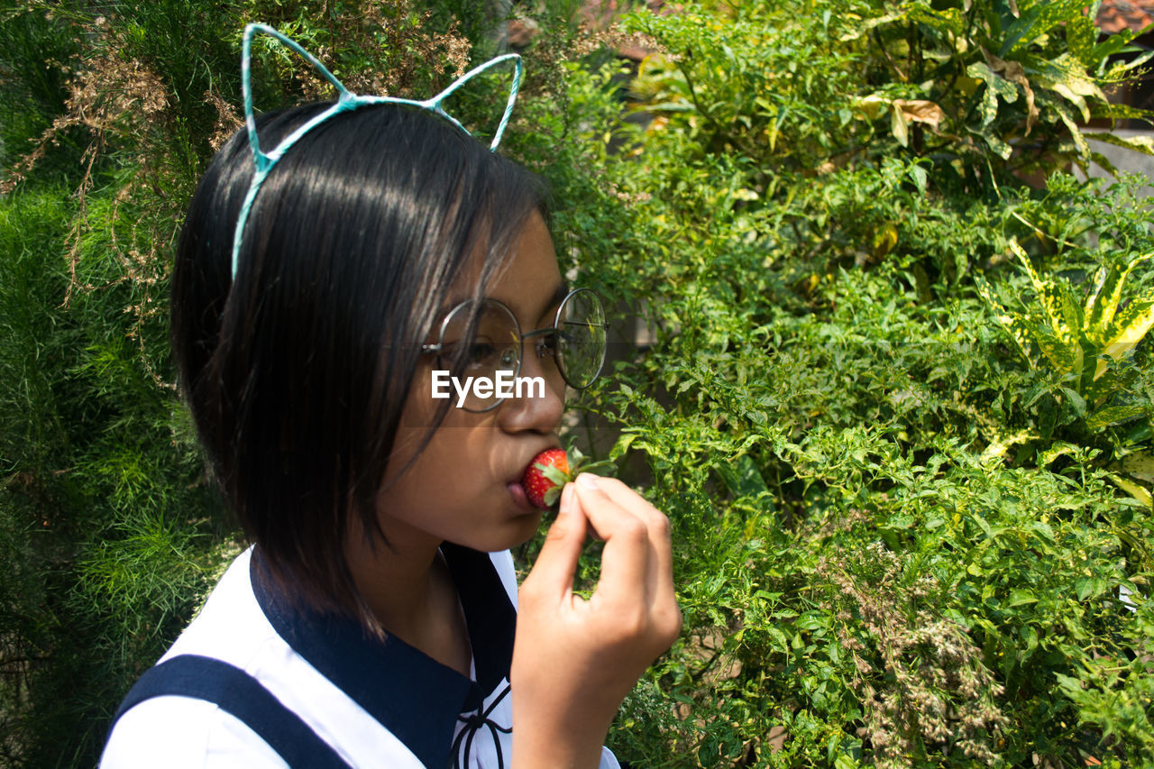 Close-up of girl eating strawberry while standing by plant