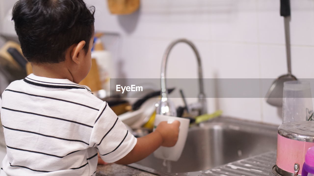 Rear view of boy with faucet in water at home