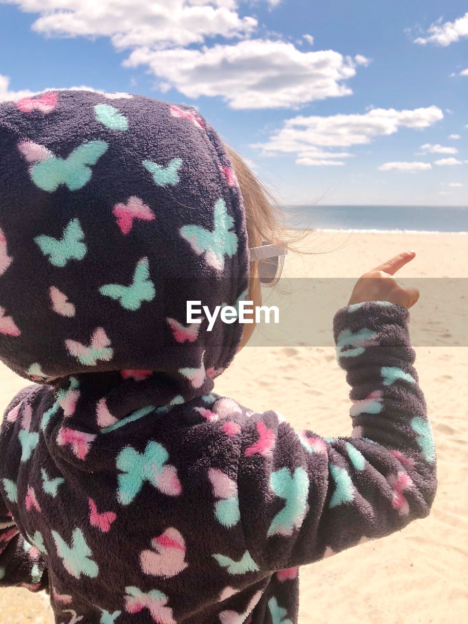 Close-up of girl pointing while wearing hooded shirt at beach