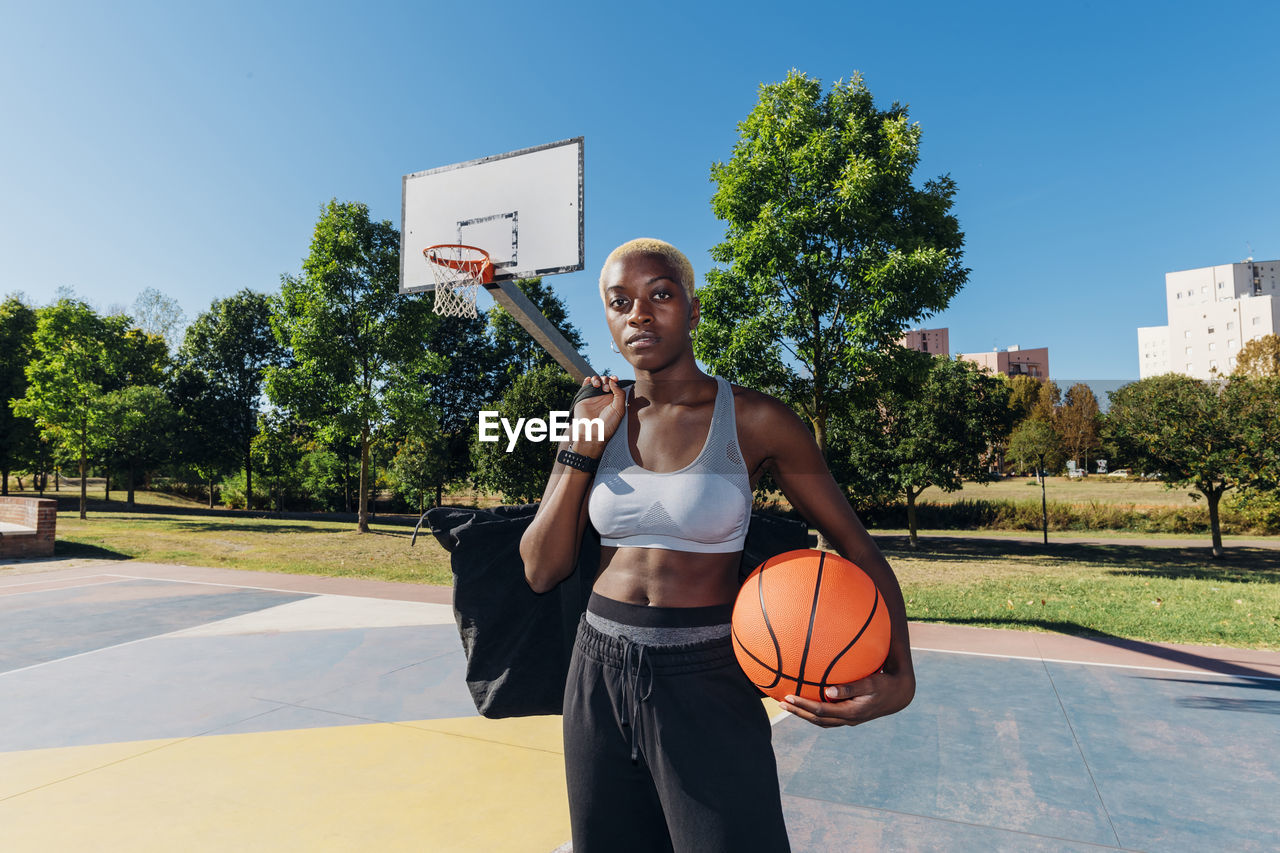 Confident basketball player with sports ball in court on sunny day