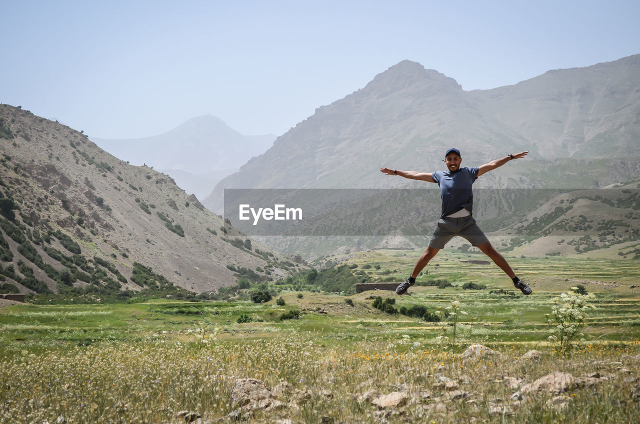 FULL LENGTH OF MAN WITH ARMS RAISED ON MOUNTAIN