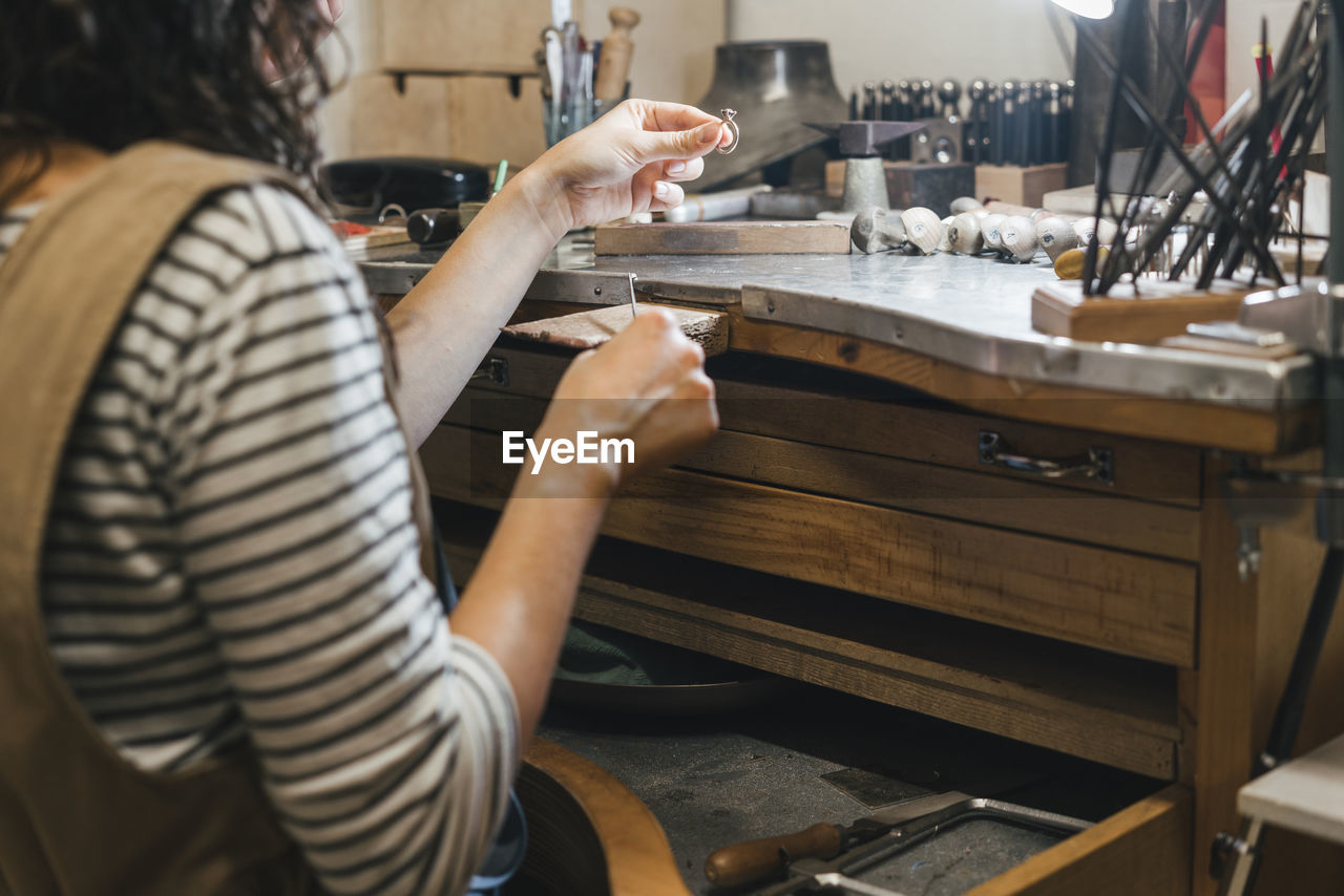 Midsection of student shaping ring while sitting by table in workshop