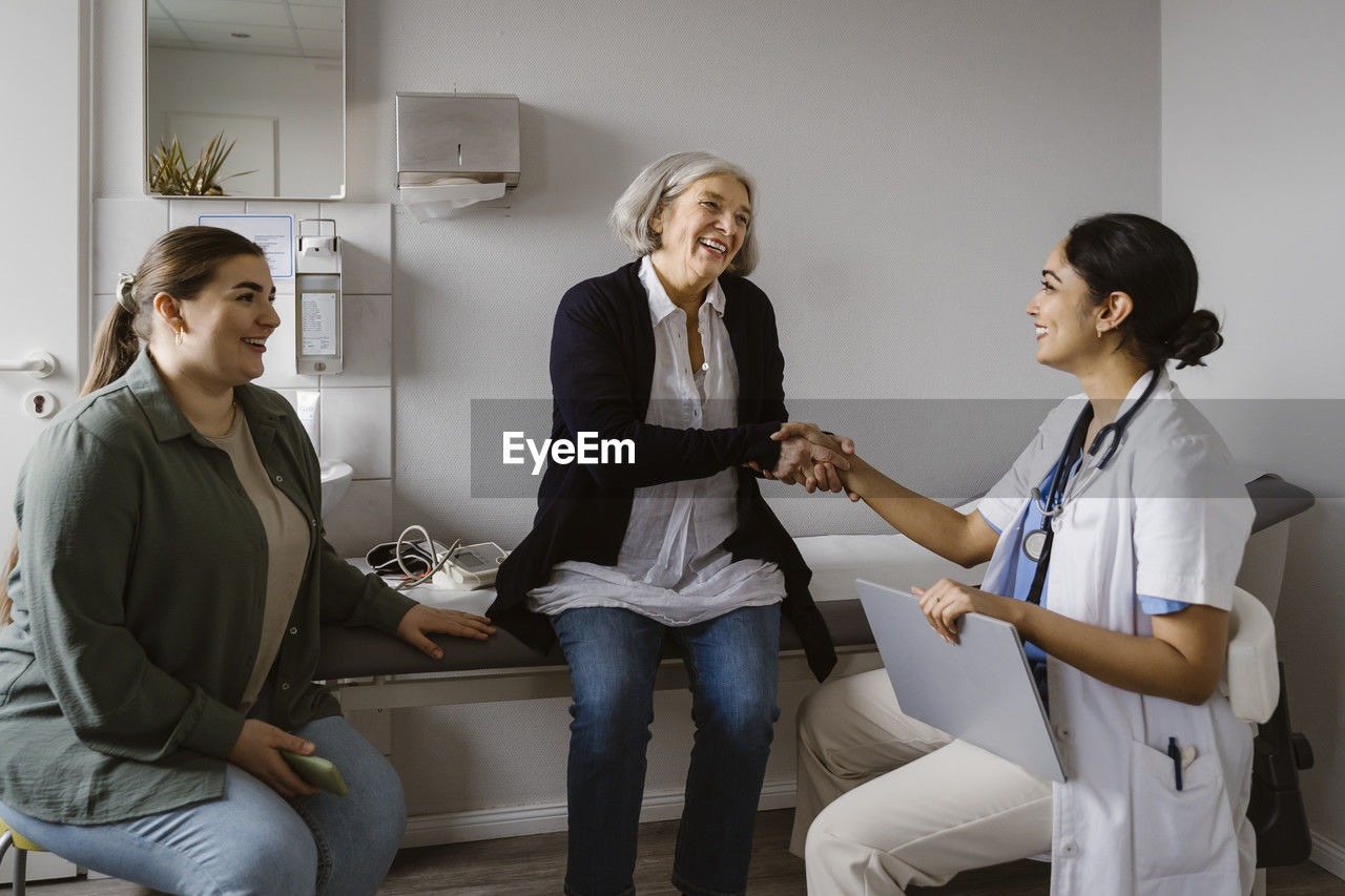 Happy senior woman shaking hand with doctor sitting in clinic