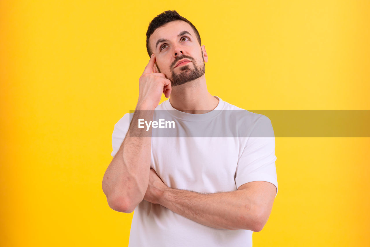yellow, adult, one person, colored background, beard, facial hair, yellow background, men, studio shot, waist up, indoors, person, young adult, portrait, casual clothing, standing, clothing, human face, front view, t-shirt, copy space, lifestyles, looking, hand, arm, emotion, finger, human hair