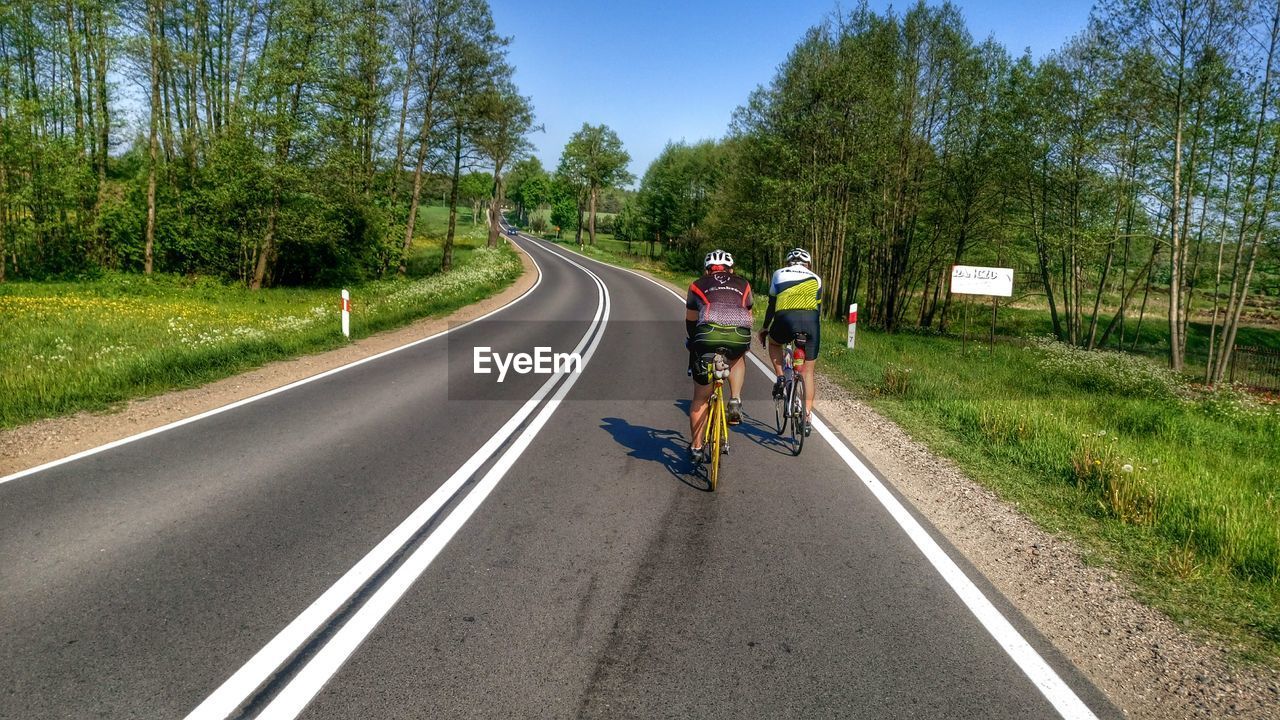 REAR VIEW OF PEOPLE RIDING BICYCLE ON ROAD