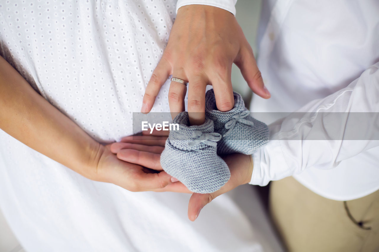 Hands of their parents, dressed in white, holding a knitted blue booties boy newborn