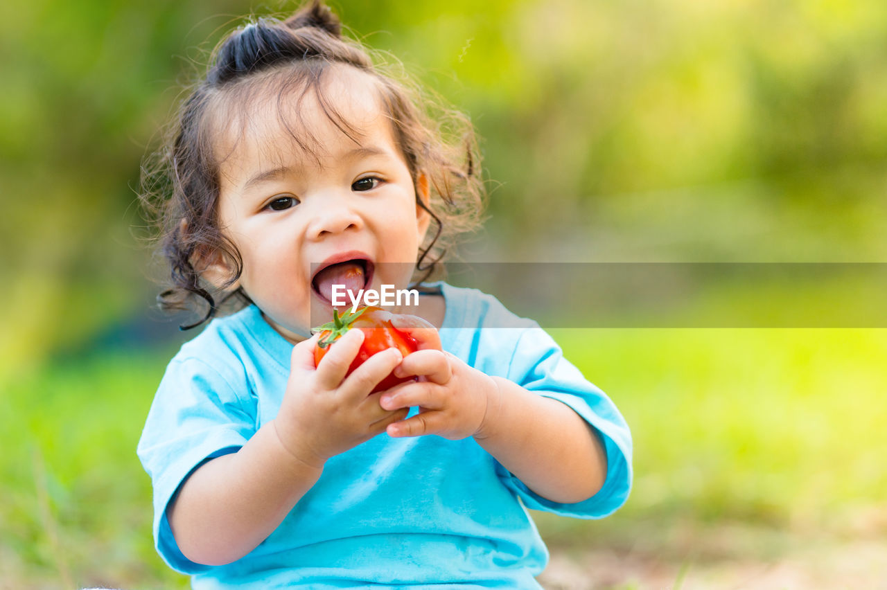 Close-up portrait of cute baby girl eating tomato on field