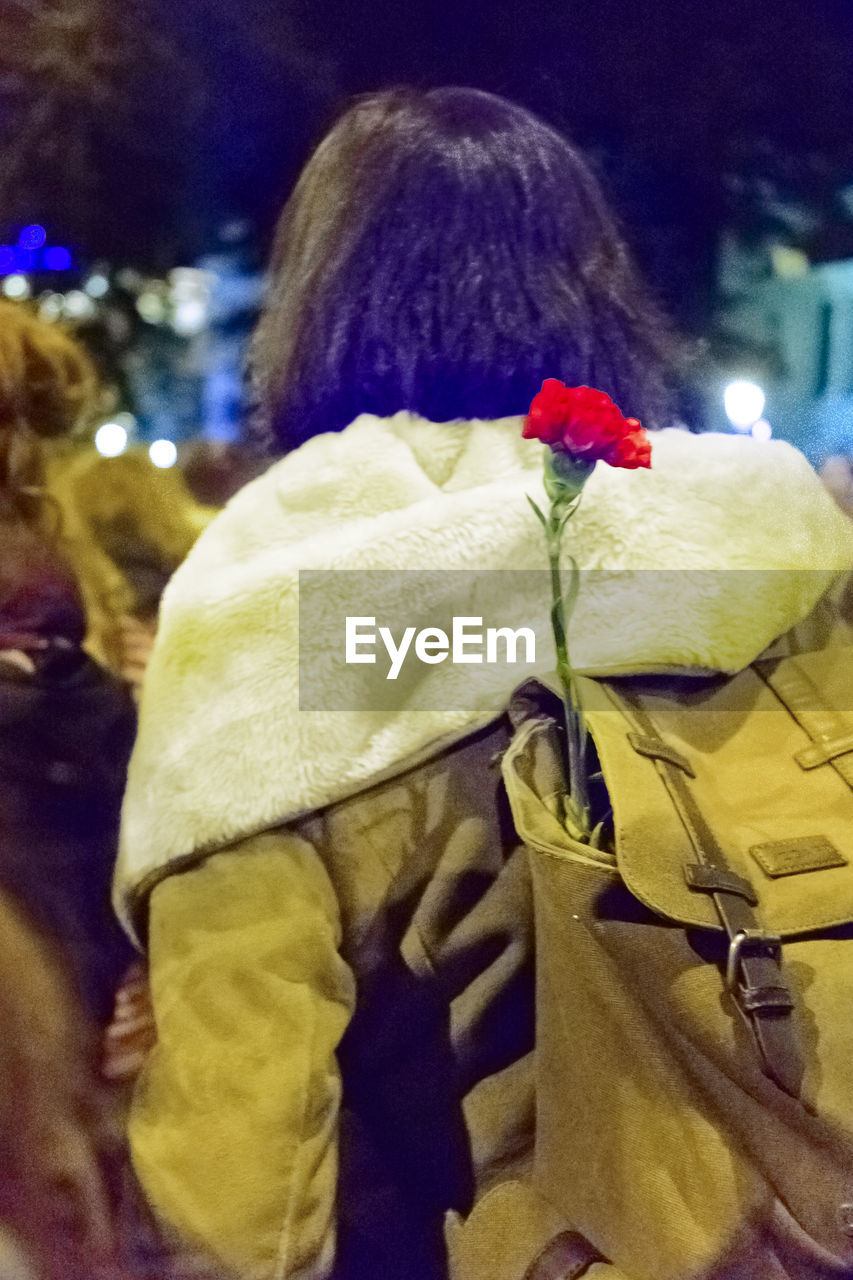 Rear view of woman with carnation flower in backpack at night