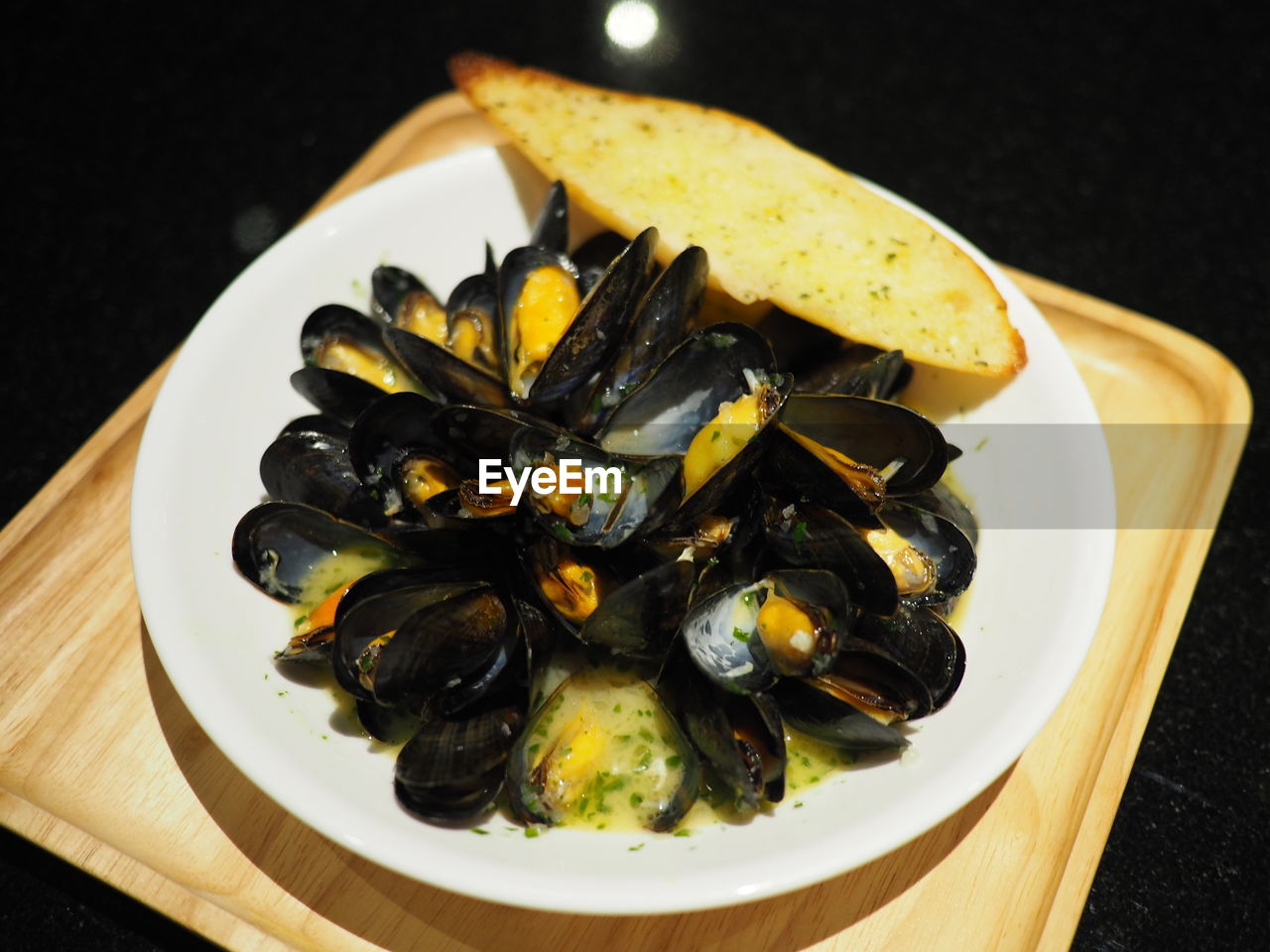 Baked mussels with cheese and garlic bread are placed on a plate.