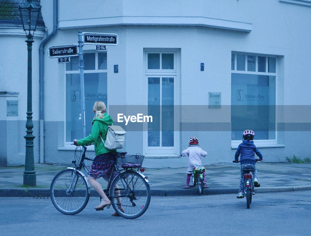 WOMAN RIDING BICYCLE ON STREET AGAINST BUILDING