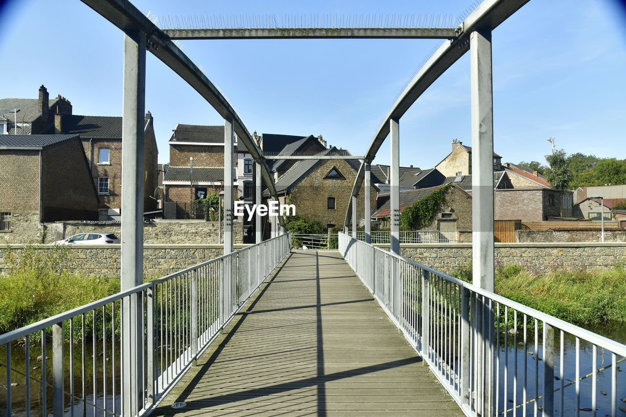 Footbridge over footpath amidst buildings against sky