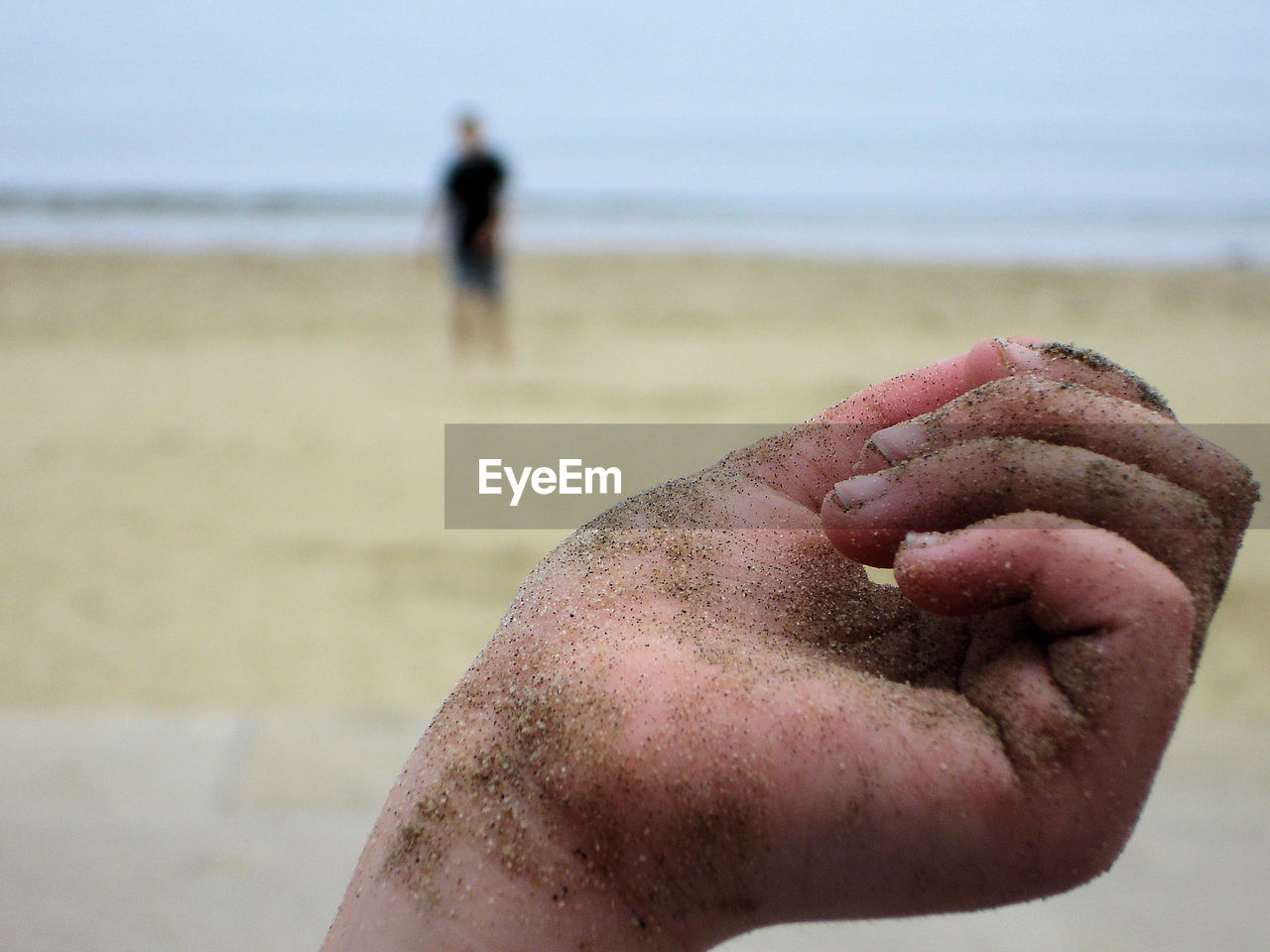 Cropped image of hand covered with sand at beach