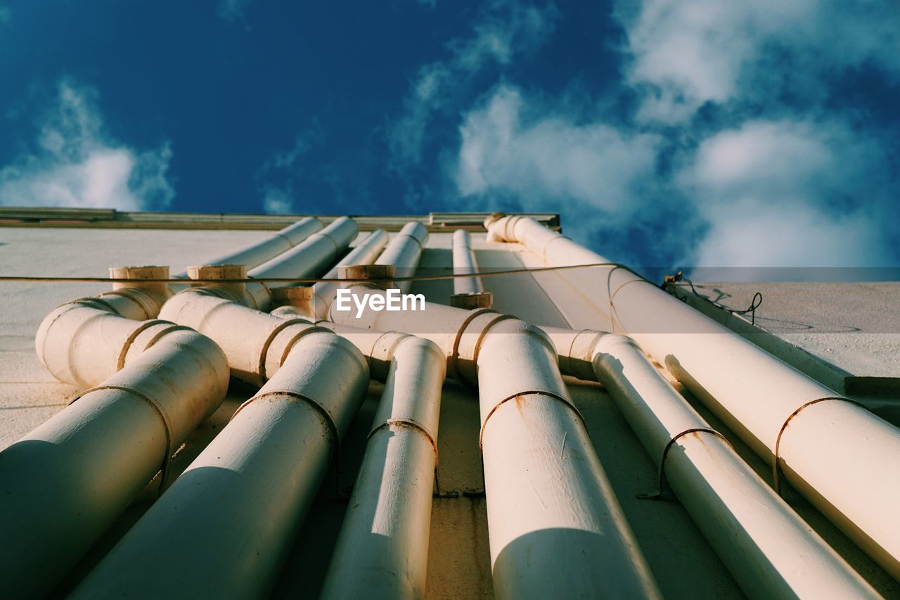 Directly below shot of pipes on building against cloudy sky