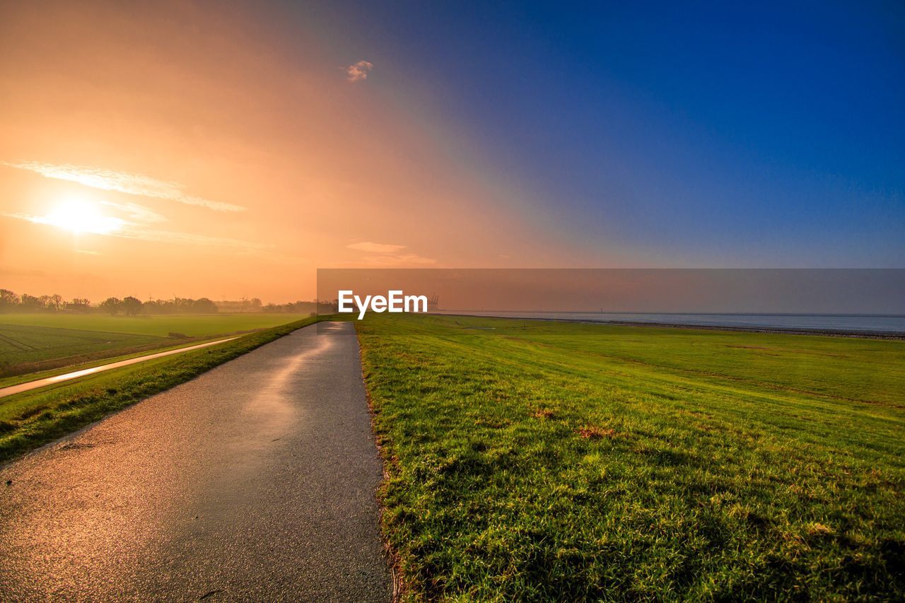 Road amidst field against sky during sunset