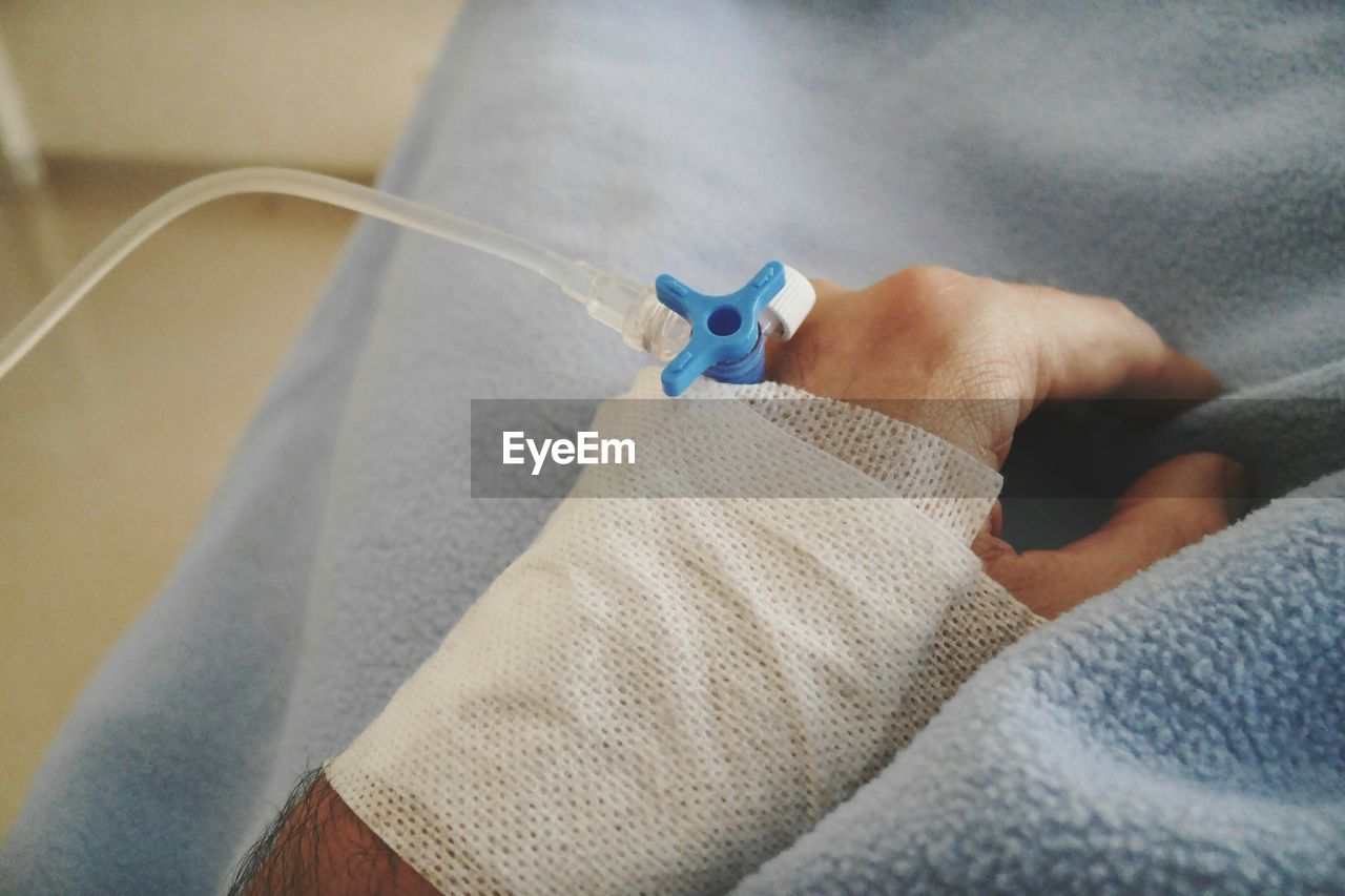 Cropped hand of patient with iv drip on bed