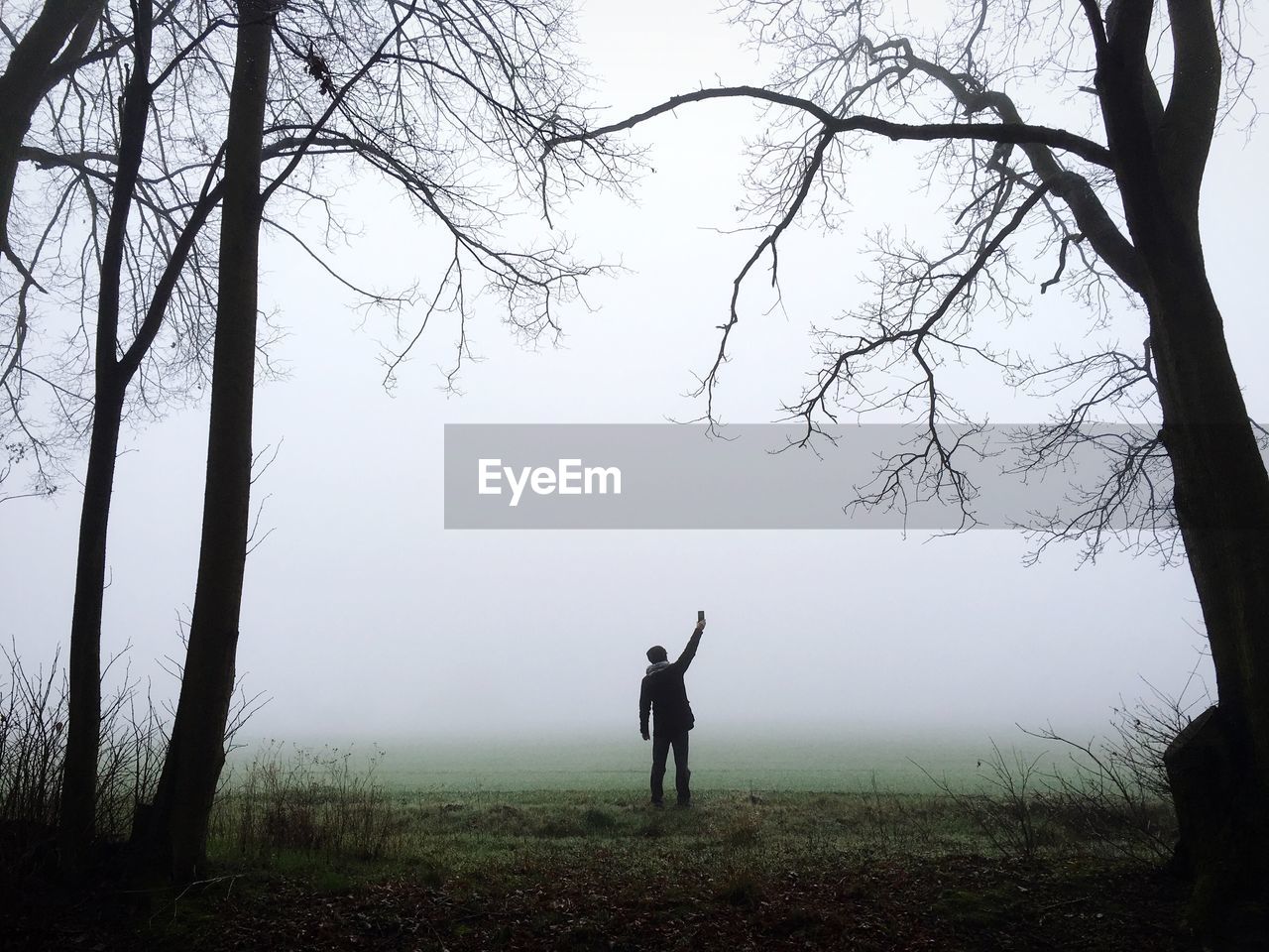 Silhouette man standing on grassy field against sky during foggy weather