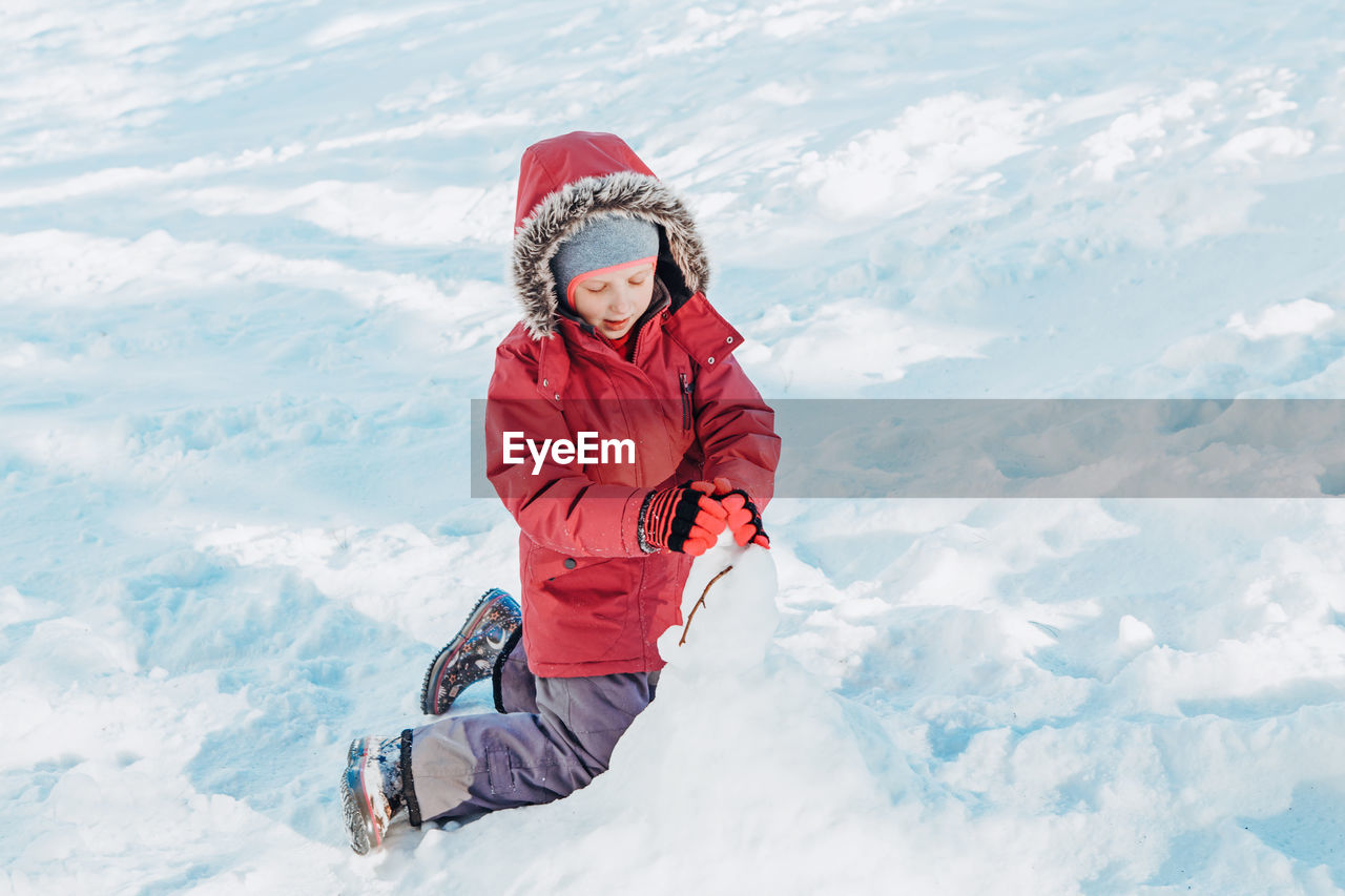  girl child in warm clothes playing with snow in park outside. kids outdoor seasonal activity.