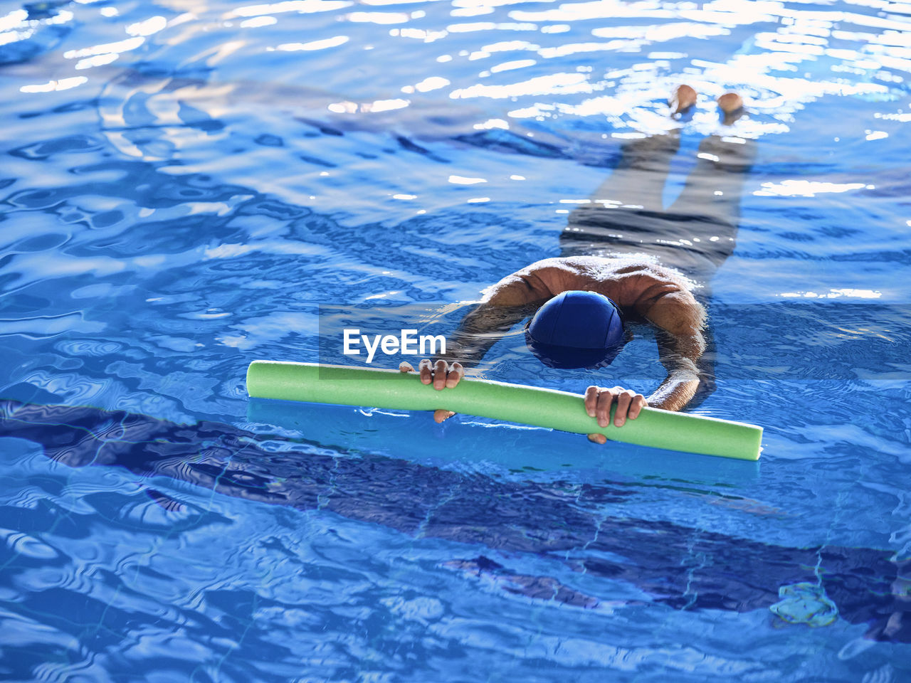 From above of anonymous female swimming with foam noodle in pool during water aerobics training