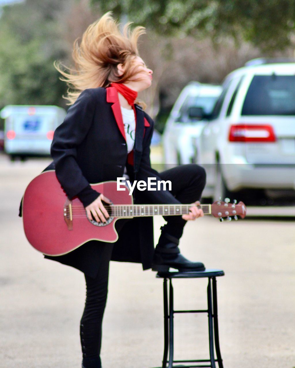 Woman playing guitar while standing on road in city