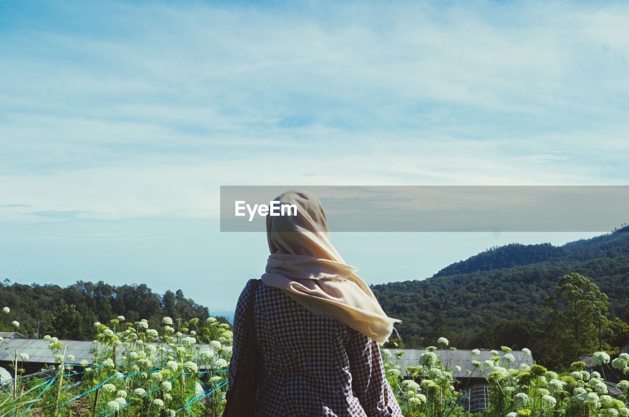 Rear view of woman standing by plants against mountains and sky