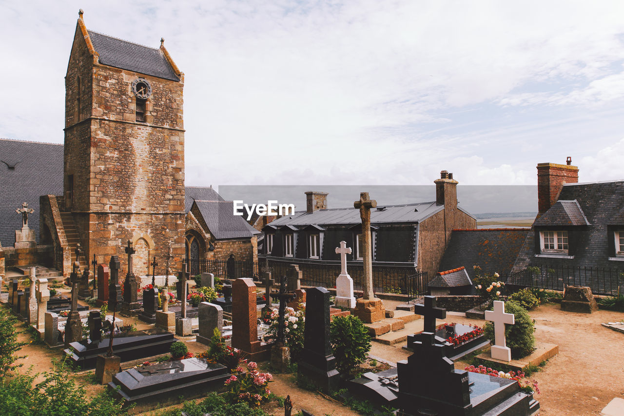 Cemetery by church against cloudy sky