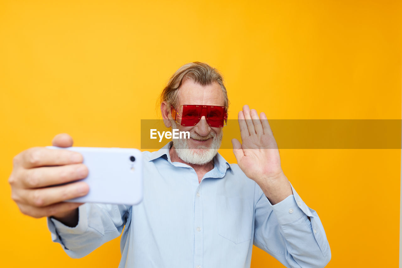 Senior man doing selfie against yellow background