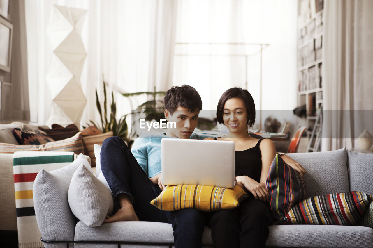 Young couple using laptop while sitting on sofa at home