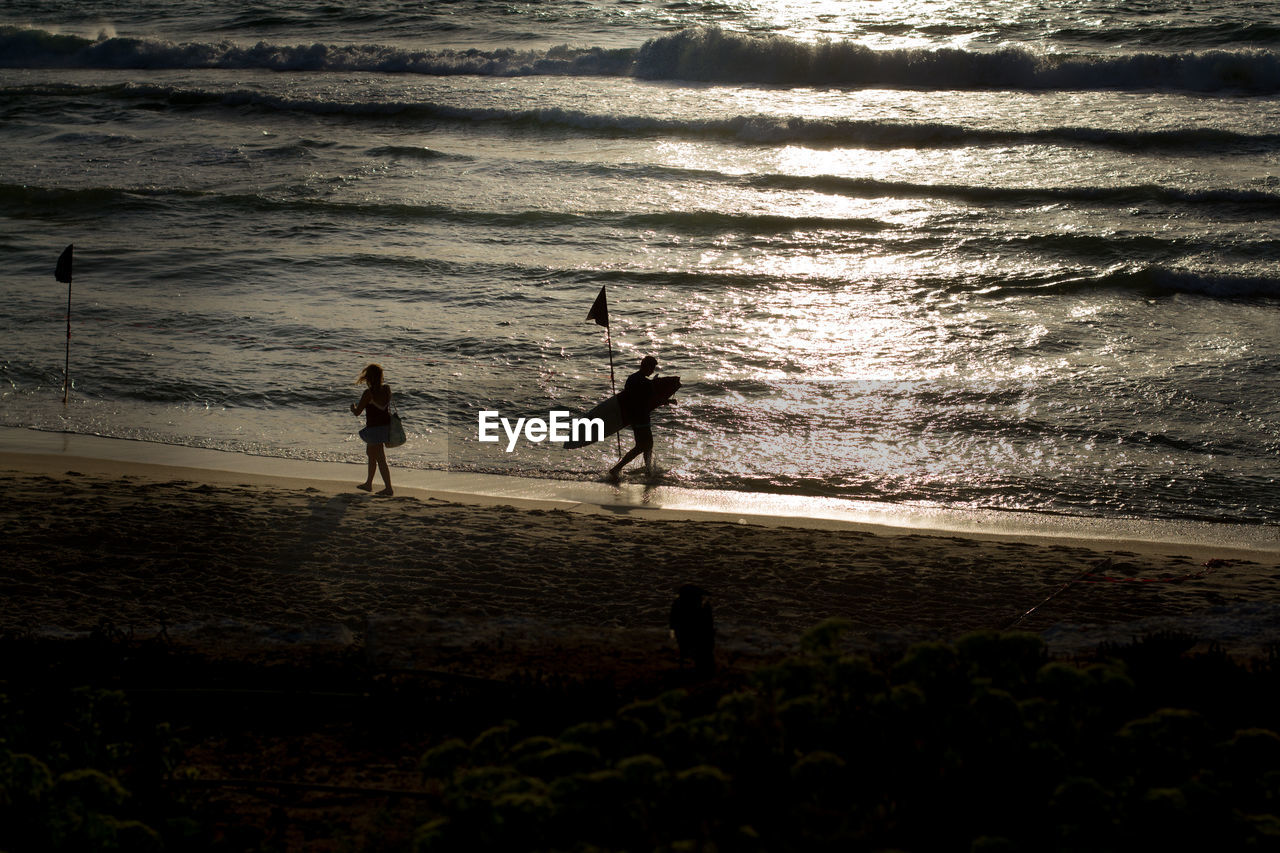 SILHOUETTE PEOPLE STANDING ON BEACH BY SEA AGAINST SKY