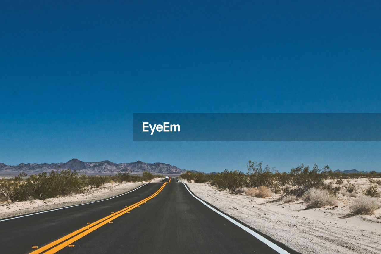 Road passing through landscape against clear blue sky