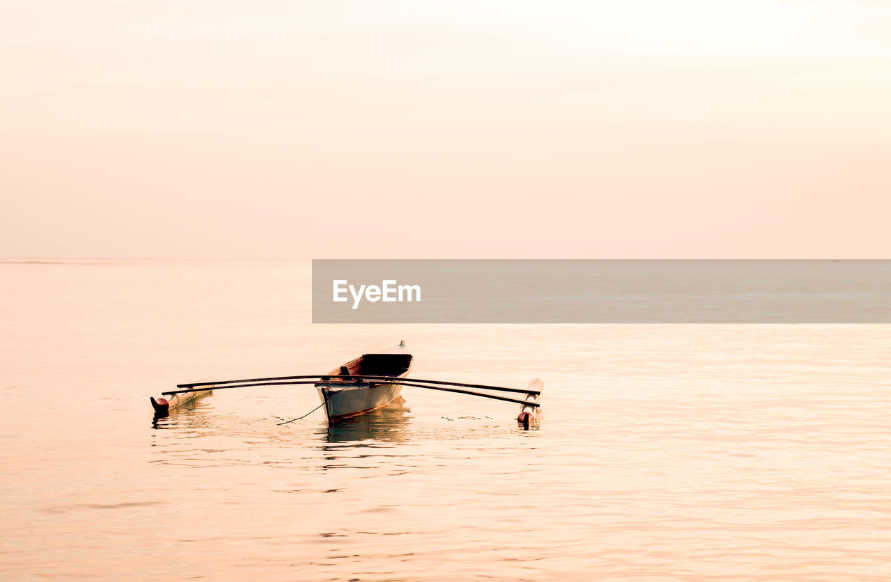 Rowing boat in sea against sky during sunset