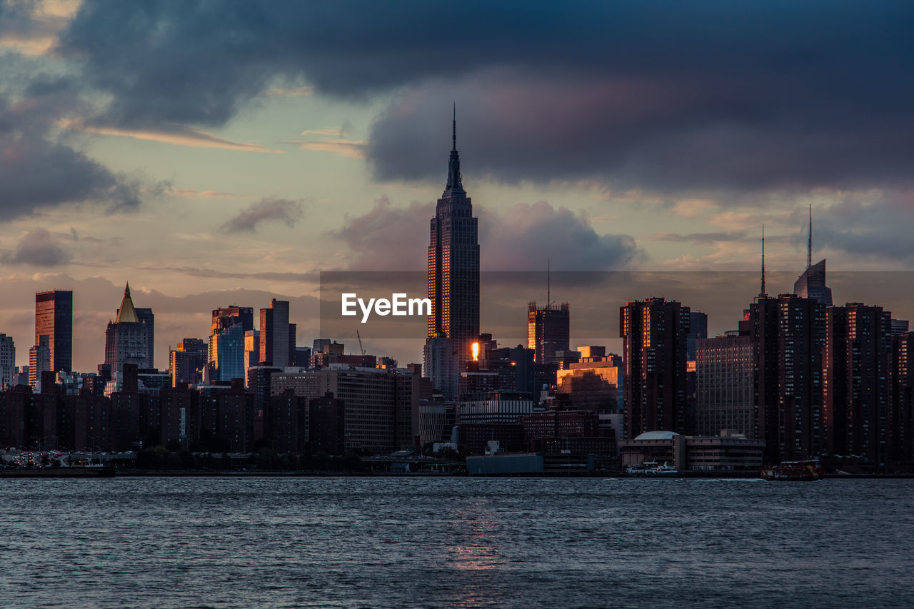 Empire state building and east river against sky during sunset in city