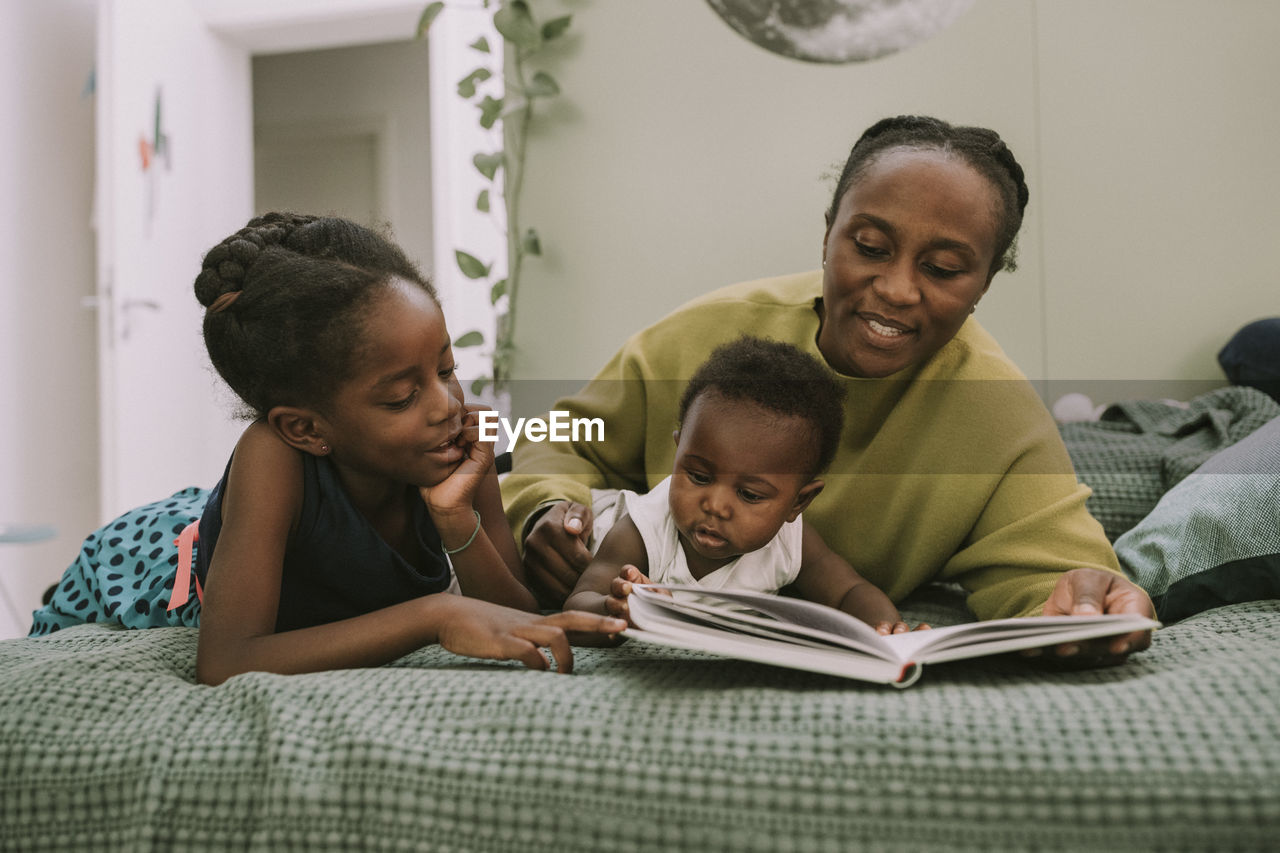 Mother with children reading book lying on bed at home