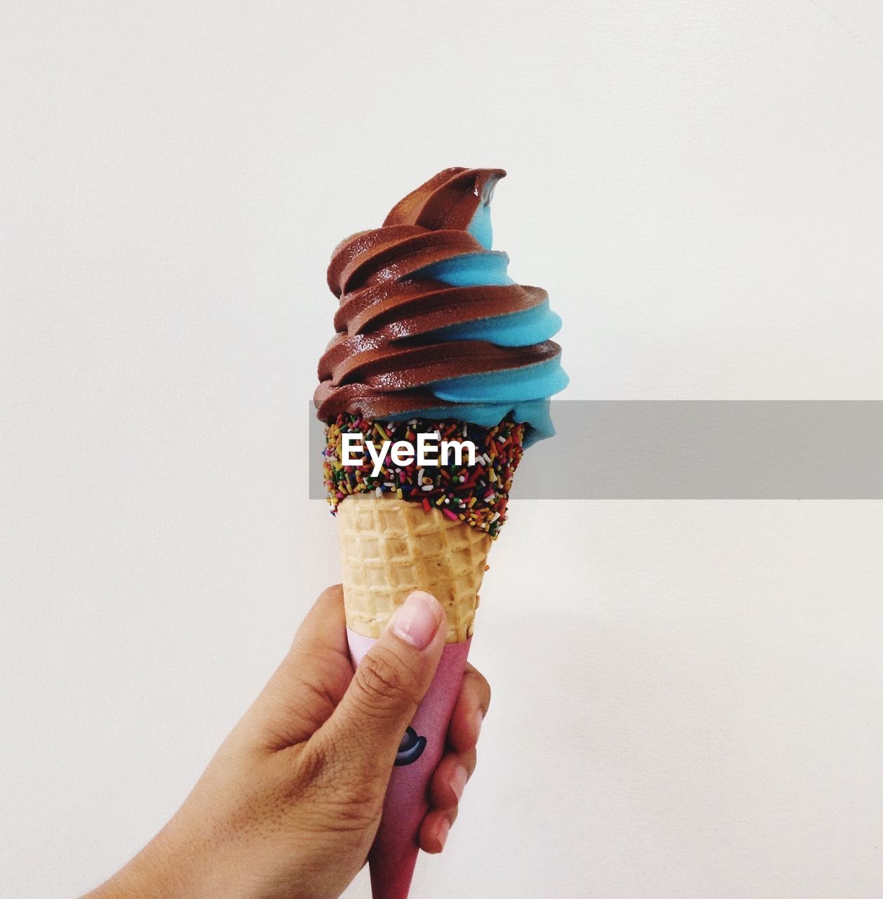 Close-up of hand holding ice cream cone over white background