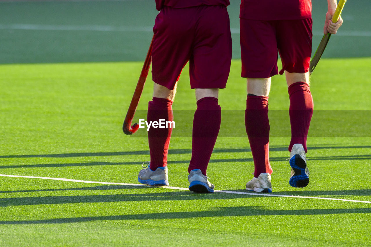 Rear view low section of hockey players walking on playing field