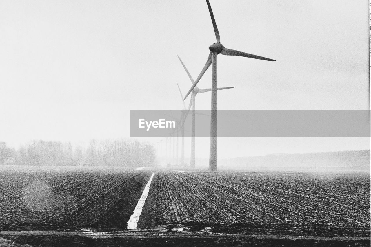 Windmills on field against sky during foggy weather