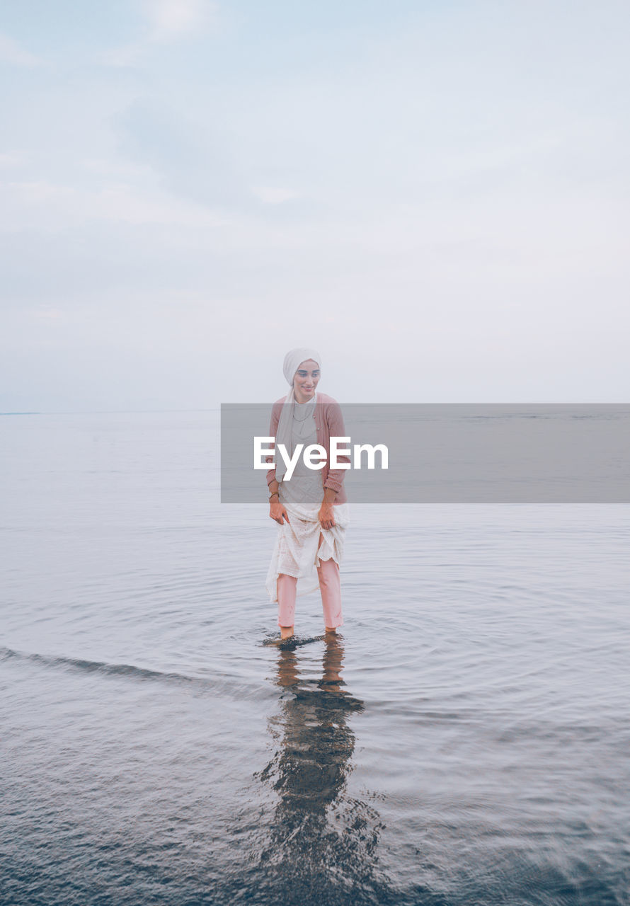 Woman wading in sea against sky