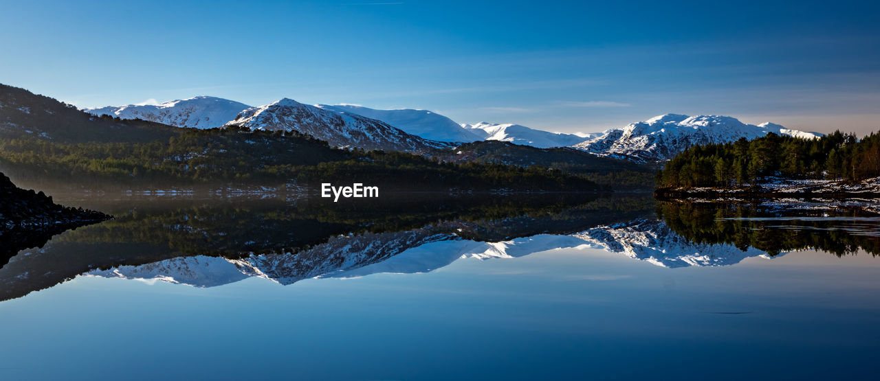 Scenic view of lake and mountains against clear blue sky