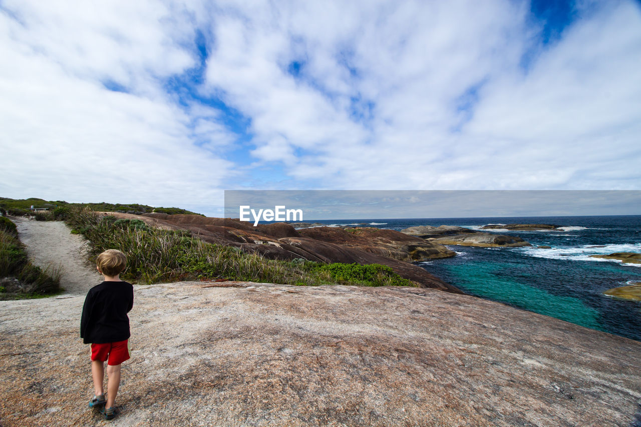 Rear view of boy standing on rocks against cloudy sky