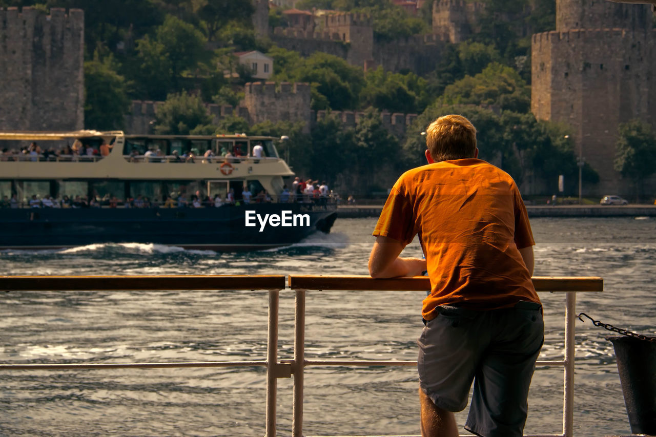 Rear view of man standing on ferry at lake